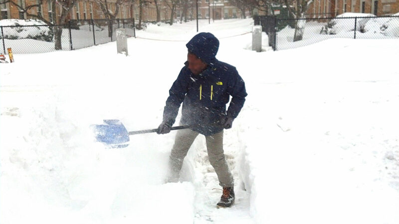 ボストンの住宅前でシャベルを使って雪かきをする様子